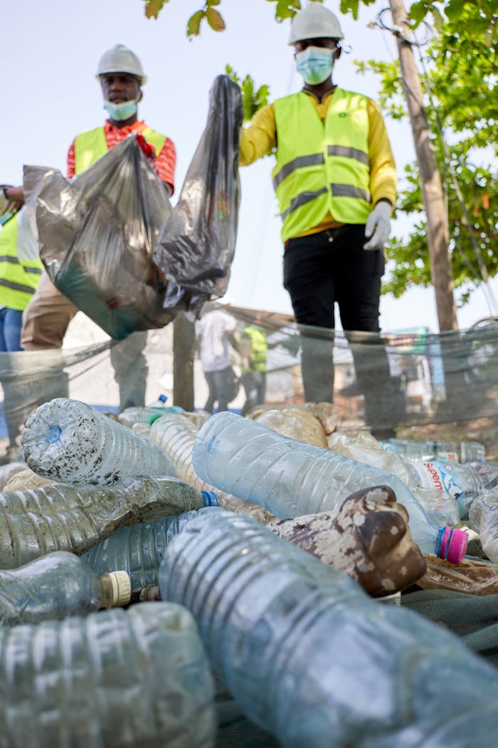 Workers in reflective vests collect plastic bottles during an outdoor cleanup effort.